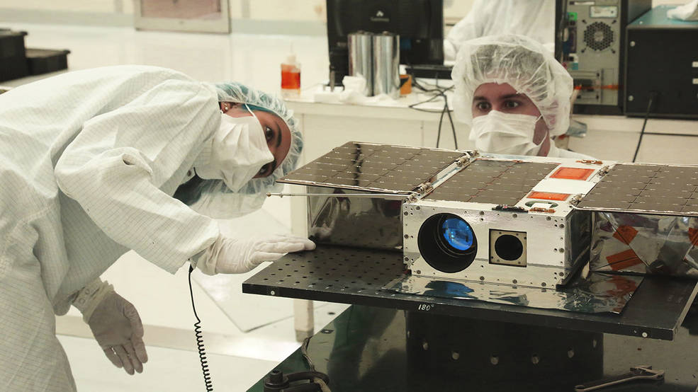 A small satellite called ASTERIA is seen in the clean room with two engineers