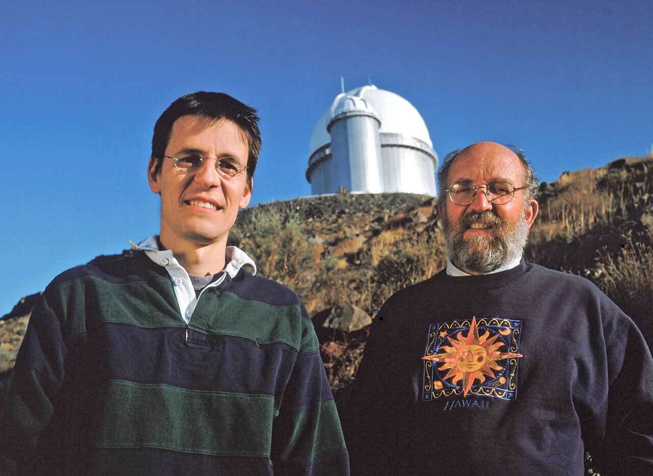 Two astronomers in front of an observatory on a bright day.