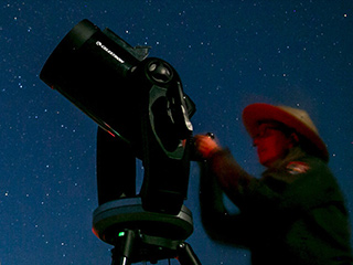 A park ranger at Dinosaur National Monument adjusts a telescope during a night sky program, with a star filled sky behind her.