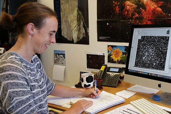 Photo of Ann Marie Cody at her desk with a space image on her monitor.