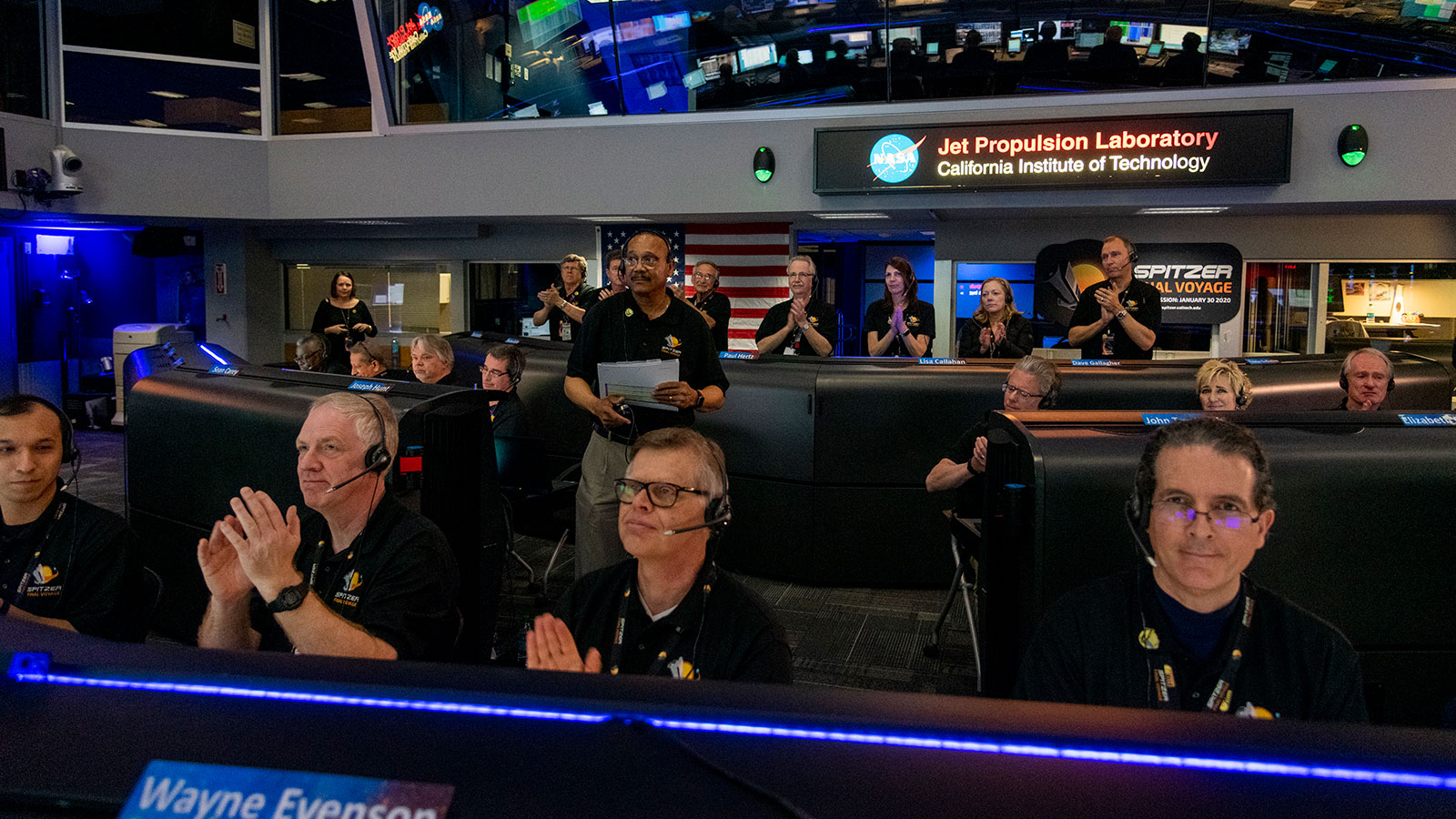 Men and women applauding in mission control as Spitzer's mission is declared over.