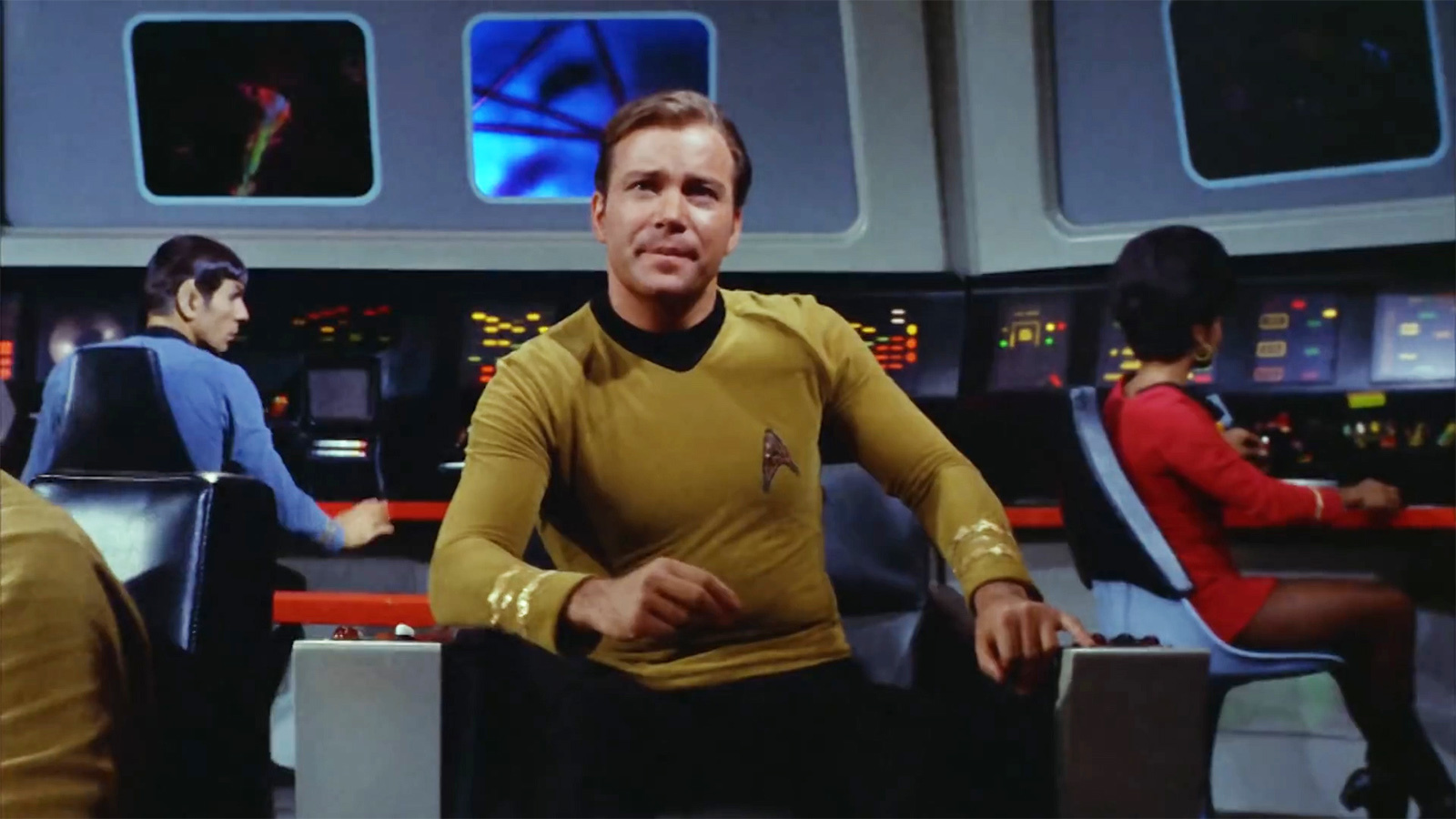 Captain Kirk sits in his chair on the bridge of the U.S.S. Enterprise.