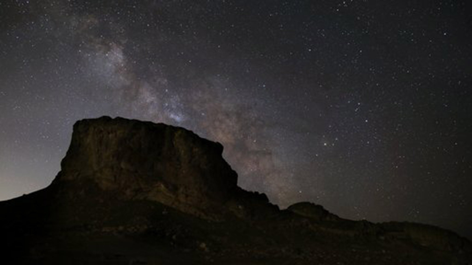 A picture of the night sky in Skull Valley Utah from June 2021 shows the constellation Scorpius to the upper right of the silhouette of a desert butte. The dark blue sky is filled with countless bright stars. Credit: NASA/Bill Dunford